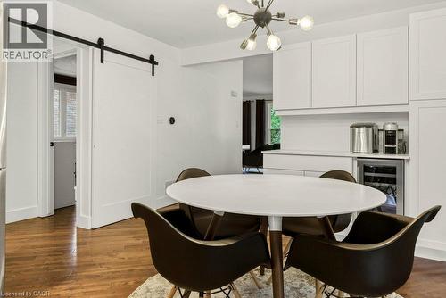 Hardwood flooring throughout, white cabinetry with integrated beverage refrigerator, modern chandelier, and a white barn door - 9 Midway Street, Hamilton, ON 