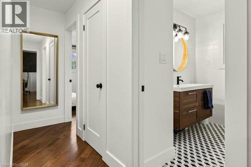 Hardwood-style flooring, white paneled doors, and a bathroom featuring geometric floor tiling, a wood-finish vanity, and subway tile walls - 9 Midway Street, Hamilton, ON 