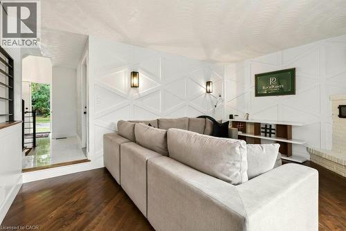 Hardwood flooring, white wall paneling, two wall sconces, white brick fireplace, and a built-in shelving unit - 9 Midway Street, Hamilton, ON 