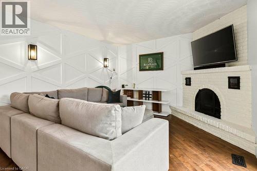Wood-finish flooring, white brick fireplace, decorative wall paneling, and wall-mounted light fixtures - 9 Midway Street, Hamilton, ON 