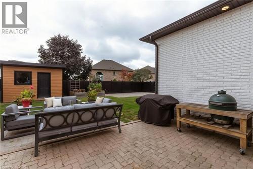 Paved patio area, white brick exterior wall, detached shed with wood-finish siding, backyard with green lawn, and dark fence - 9 Midway Street, Hamilton, ON 