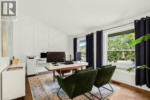 White accent wall with geometric paneling, two large windows, wood-finish flooring, and sloped ceiling - 9 Midway Street, Hamilton, ON 