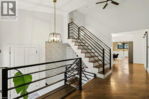 Wood-finish flooring throughout, modern open-riser staircase with black metal railings, contemporary ceiling fan, and decorative wall paneling - 9 Midway Street, Hamilton, ON 