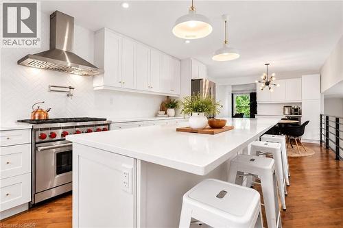 Kitchen featuring white cabinetry, a large center island with a light-toned countertop, stainless steel range with a pot filler, coordinating range hood, and wood-finish flooring - 9 Midway Street, Hamilton, ON 