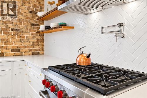 Stainless steel range with red accent knobs, white shaker-style cabinetry, white countertops, white herringbone tile backsplash, and a wall-mounted pot filler - 9 Midway Street, Hamilton, ON 