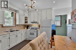 White cabinetry with brushed nickel hardware, stainless steel double basin sink, neutral countertops, gas range, and a contemporary brass chandelier - 