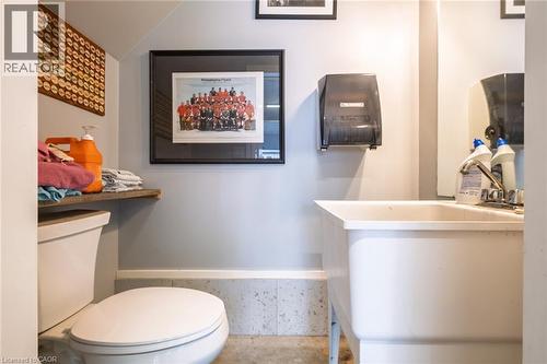 Utility room with a porcelain toilet, wall-mounted shelving, and a large utility sink with a chrome faucet - 78 Oak Street, Simcoe, ON 