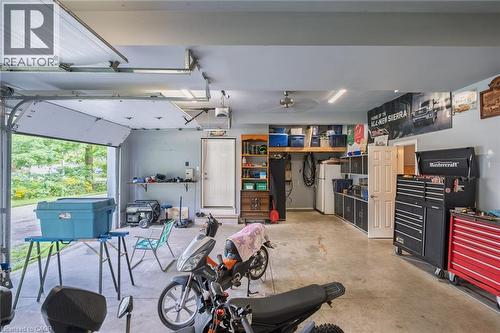 Attached garage with an overhead door, smooth concrete flooring, built-in shelving, and a pedestrian door - 78 Oak Street, Simcoe, ON 
