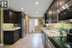 Contemporary kitchen featuring dark wood cabinetry, stainless steel appliances, light-toned countertops, and recessed lighting - 