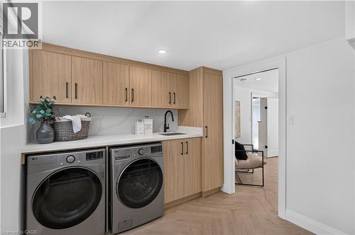 Integrated laundry area featuring wood-finish cabinetry, a white countertop, a black faucet, and a herringbone-patterned floor - 3028 Eva Drive, Burlington, ON 