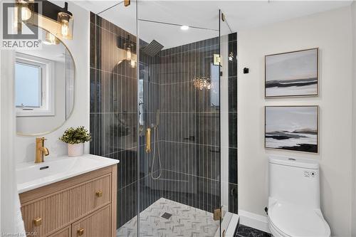 Glass-enclosed shower with vertical dark tile surround, gold-finish fixtures, and patterned floor tile - 3028 Eva Drive, Burlington, ON 