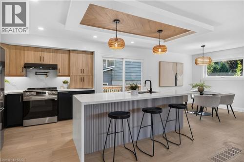 Kitchen featuring wood-finish upper cabinetry, black lower cabinetry, stainless steel range, and a waterfall island with a fluted panel base - 3028 Eva Drive, Burlington, ON 