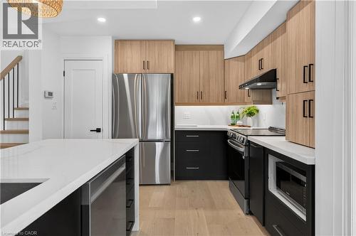Kitchen featuring light wood-finish upper cabinetry, black lower cabinetry, stainless steel appliances, and white countertops - 3028 Eva Drive, Burlington, ON 