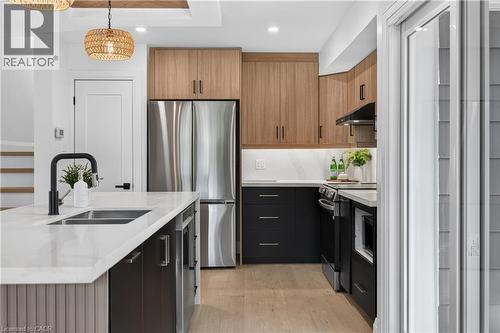 Kitchen featuring stainless steel appliances, wood-finish cabinetry, a large center island with a sink, and light wood-finish flooring - 3028 Eva Drive, Burlington, ON 