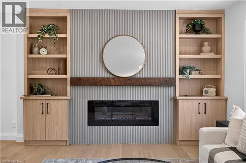 Built-in shelving with lower cabinetry, reeded accent wall, wood-finish mantel, and an electric fireplace - 3028 Eva Drive, Burlington, ON 