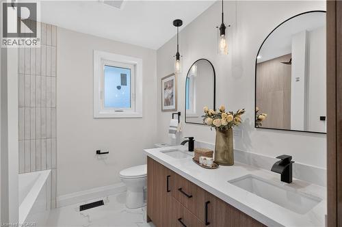 Dual arched mirrors, dual undermount sinks, wood-finish vanity, matte black fixtures, and vertical tile shower surround - 3028 Eva Drive, Burlington, ON 