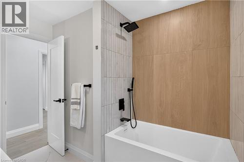 Deep soaking tub with matte black fixtures, textured wood-finish accent wall, and vertical-stacked tile surround - 3028 Eva Drive, Burlington, ON 