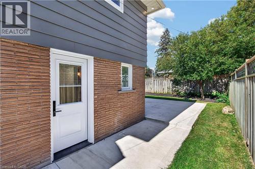 Concrete patio with a white entry door, brick siding, and wood fencing - 3028 Eva Drive, Burlington, ON 