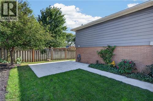 Expansive lawn area with a concrete patio, wood-finish privacy fencing, mature trees, and a brick and siding exterior - 3028 Eva Drive, Burlington, ON 