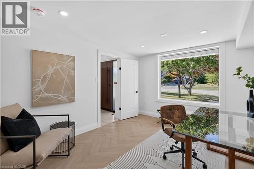 Recessed lighting illuminates the room, featuring wood-finish flooring in a herringbone pattern and a large window - 3028 Eva Drive, Burlington, ON 