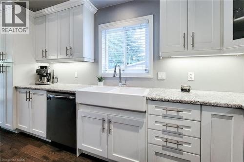 White shaker cabinetry, light-toned countertops, a farmhouse-style sink with a gooseneck faucet, a built-in dishwasher, and wood-finish flooring - 4274 Sixth Avenue, Niagara Falls, ON 