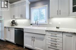 White shaker cabinetry, light-toned countertops, a farmhouse-style sink with a gooseneck faucet, a built-in dishwasher, and wood-finish flooring - 