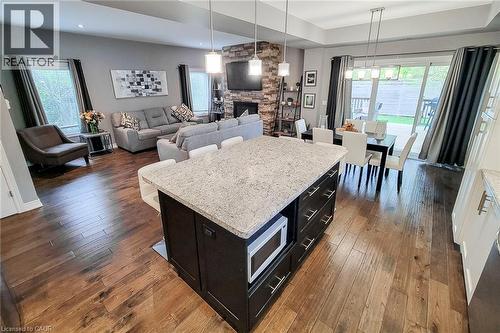 Open-concept living space with wood-finish flooring, a stone-clad fireplace, and a large kitchen island with a light-toned countertop - 4274 Sixth Avenue, Niagara Falls, ON 