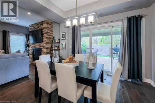 Wood-finish flooring throughout, a stone-accented fireplace, a ceiling tray, and a sliding glass door leading to an outdoor deck - 4274 Sixth Avenue, Niagara Falls, ON 