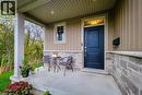 Covered front porch featuring a dark paneled entry door, stone and vertical siding exterior, and a single pane window - 4274 Sixth Avenue, Niagara Falls, ON 