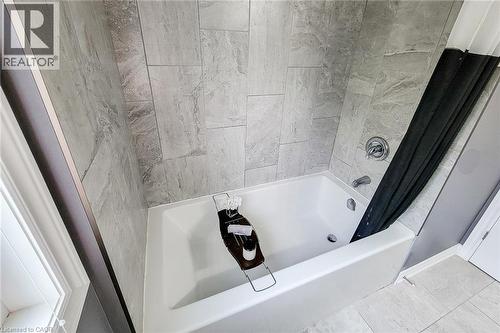 White soaking tub with chrome fixtures, surrounded by large format gray tile - 4274 Sixth Avenue, Niagara Falls, ON 