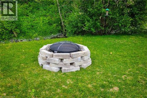 Lawn area featuring a built-in stone block fire pit with a mesh cover, bordered by dense green foliage - 4274 Sixth Avenue, Niagara Falls, ON 
