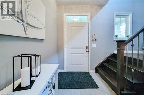 Entryway featuring a solid wood door with transom window, light wood-finish flooring, and a dark wood staircase with wrought iron balusters - 4274 Sixth Avenue, Niagara Falls, ON 