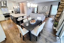 Open-concept main living area with wood-finish flooring, a kitchen island with seating, stainless steel appliances, a stacked stone accent wall, and recessed lighting - 