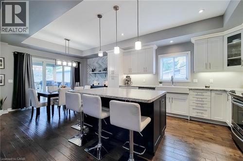 Kitchen featuring a center island with bar seating, white perimeter cabinetry, stone countertops, and a farmhouse-style sink - 4274 Sixth Avenue, Niagara Falls, ON 