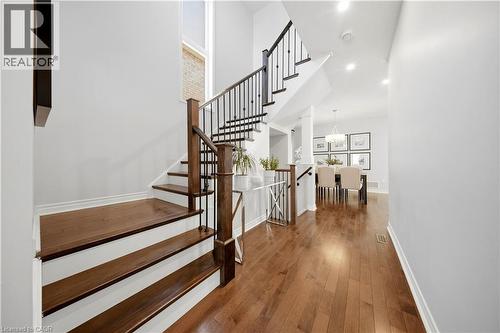 Hardwood flooring, wood-finish stairs with white risers, wrought iron and wood railings, recessed lighting, and a chandelier in the background - 3352 Hiscott Avenue, Burlington, ON 
