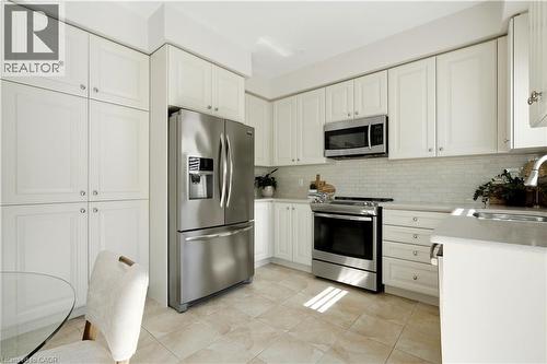 Kitchen featuring white cabinetry, stainless steel appliances, subway tile backsplash, and light-toned tile flooring - 3352 Hiscott Avenue, Burlington, ON 
