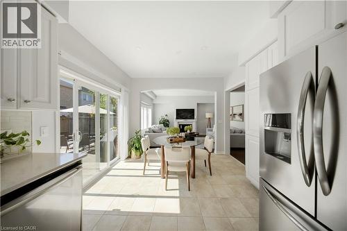 Stainless steel refrigerator, white shaker-style cabinetry, light-toned tile flooring, light-toned countertop, and sliding glass patio doors - 3352 Hiscott Avenue, Burlington, ON 