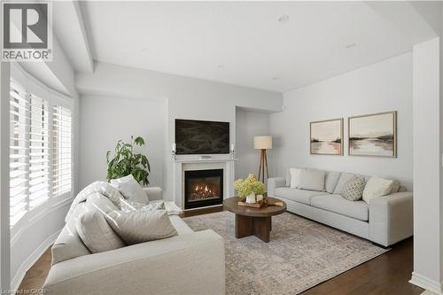 Living area featuring wood-finish flooring, a fireplace with a white mantel, and a bay window with white plantation shutters - 3352 Hiscott Avenue, Burlington, ON 