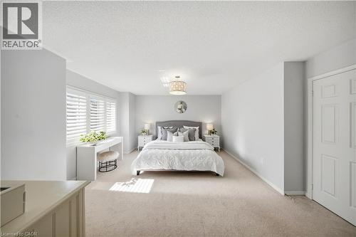 Carpeted bedroom with a built-in window desk, plantation shutters, and a central chandelier - 3352 Hiscott Avenue, Burlington, ON 