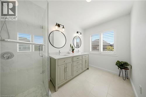 Spacious bathroom featuring a glass-enclosed shower, dual vanity with undermount sinks, and windows with louvered shutters - 3352 Hiscott Avenue, Burlington, ON 