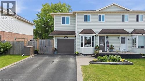 Light-colored siding exterior with a dark roof, featuring a bay window, an attached single-car garage, a paved driveway, and a front porch - 4804 John Street, Beamsville, ON 