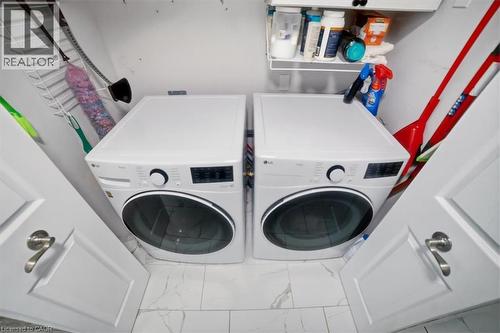 Laundry closet with white front-load washer and dryer, tile flooring, and integrated shelving - 4804 John Street, Beamsville, ON 
