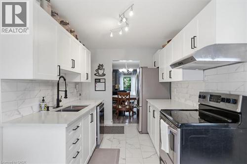 White shaker-style cabinetry with black hardware, stainless steel appliances, a subway tile backsplash, and a double basin sink with a matte black gooseneck faucet - 4804 John Street, Beamsville, ON 