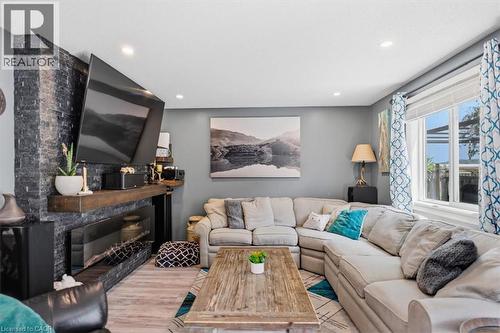 Living area featuring a floor-to-ceiling stone-look fireplace surround, a large window, recessed lighting, and wood-finish flooring - 4804 John Street, Beamsville, ON 