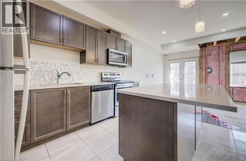 Kitchen featuring dark wood-finish cabinetry, stainless steel appliances, a white tile backsplash, and a light-toned countertop island - 403 Westwood Drive Unit# 59, Kitchener, ON 