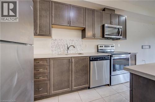 Kitchen featuring stainless steel appliances, dark wood-finish cabinetry, light-toned countertops, a tile backsplash, and tile flooring - 403 Westwood Drive Unit# 59, Kitchener, ON 