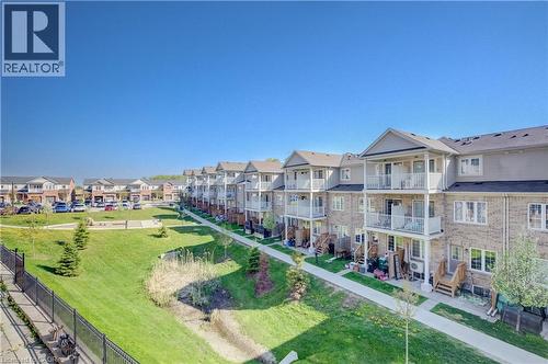 Townhome row featuring brick and siding exteriors, private balconies, individual patios, and a landscaped green space with walking paths - 403 Westwood Drive Unit# 59, Kitchener, ON 