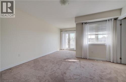 Carpeted room featuring a double French door balcony access, an additional window with white blinds, and overhead lighting - 403 Westwood Drive Unit# 59, Kitchener, ON 