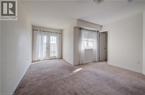 Carpeted room featuring a double French door balcony entry, a single window with blinds, and white trim - 403 Westwood Drive Unit# 59, Kitchener, ON 