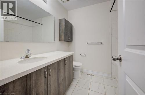 Bathroom featuring a wood-finish vanity with an integrated sink and chrome faucet, a coordinating wall-mounted storage cabinet, and white tile flooring - 403 Westwood Drive Unit# 59, Kitchener, ON 
